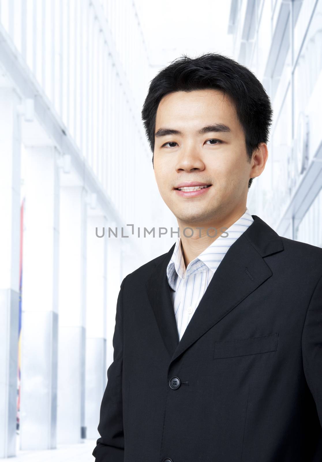 Portrait of young Asian executive in black suit, standing in front of a modern building
