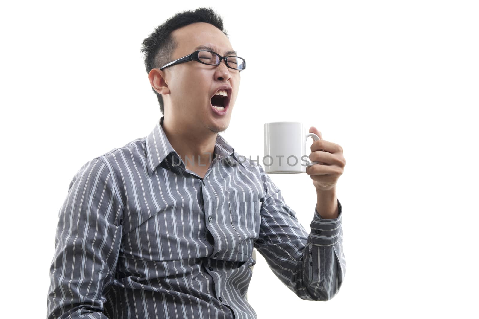 Yawning Asian male holding a cup of coffee isolated on white background