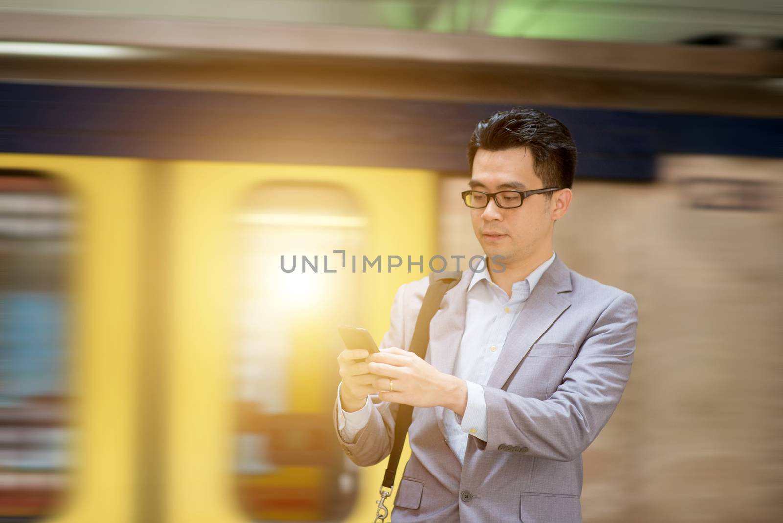 Asian businessman texting using smartphone while waiting train at railway station.