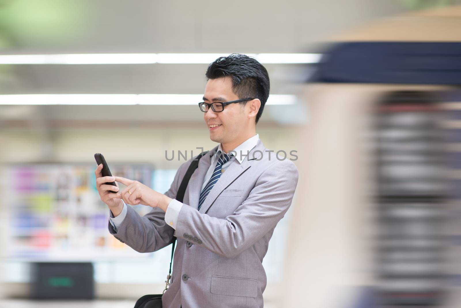 Asian business man using smart phone in subway station, train passing by at the background.
