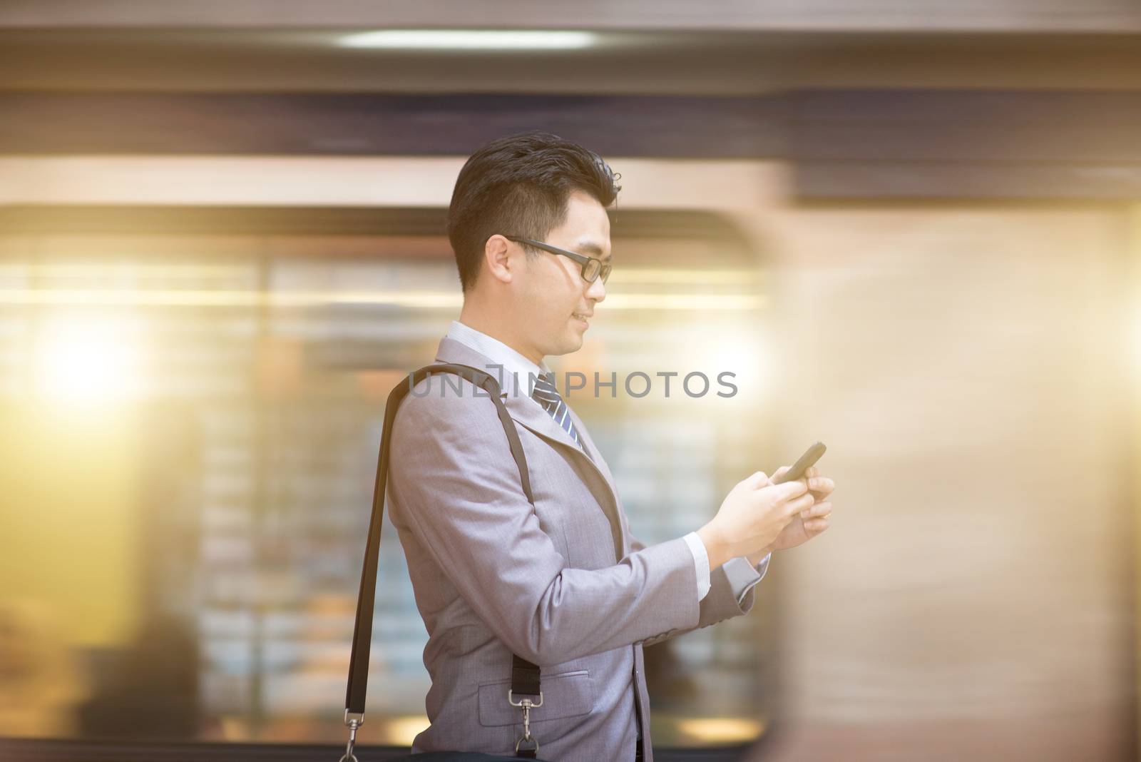 Asian businessman hand using smart phone in subway station, train passing by at the background.