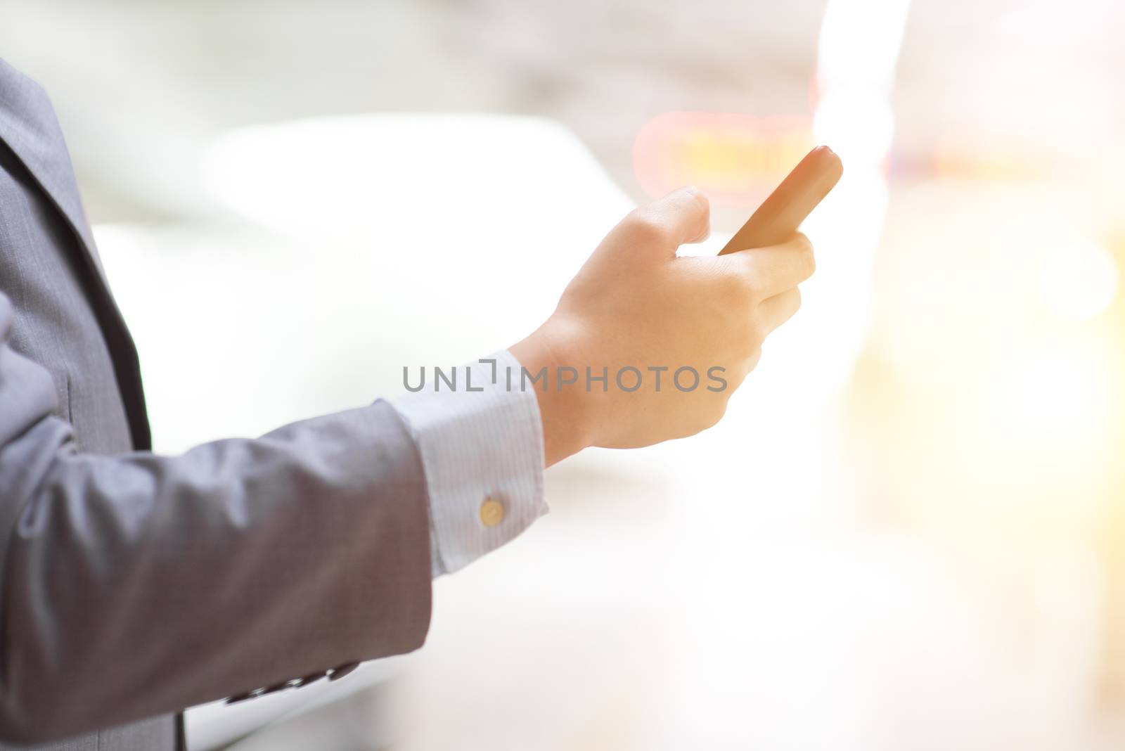 Business people using smart phone outdoors, focus on hand, bright sun flare background.