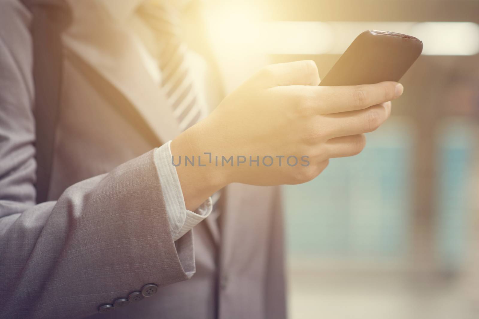 Businessman hand using smartphone at train station, with beautiful sun flare at background.