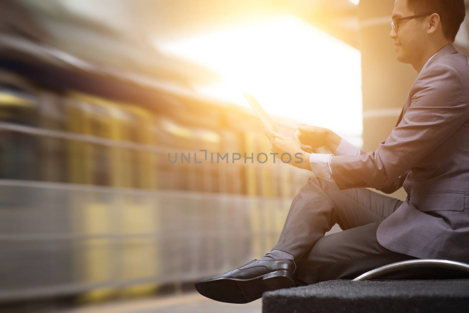Asian businessman using digital tablet pc at railway station, with beautiful sun flare at background.