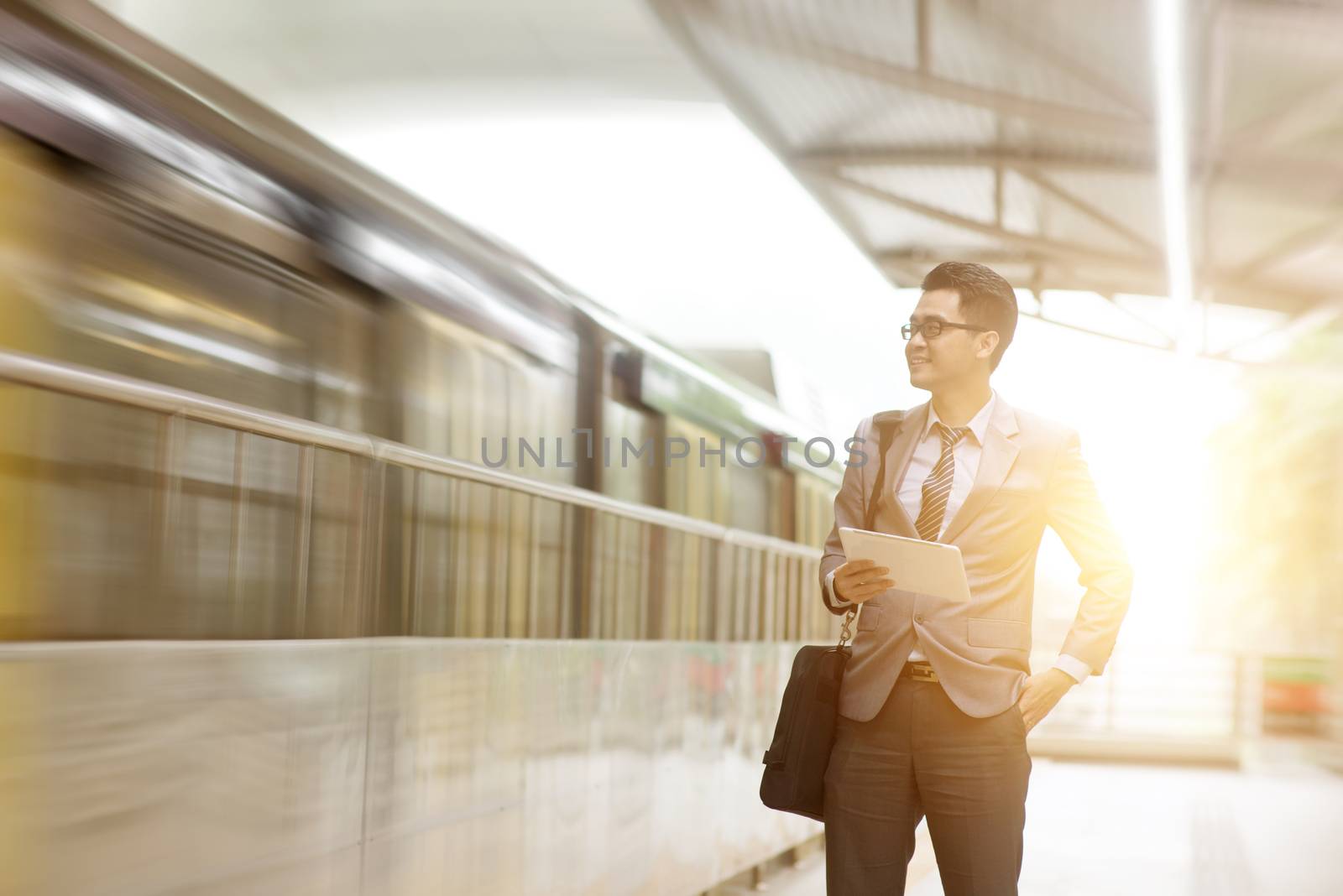 Asian businessman using digital tablet pc at commuter platform, with beautiful sun flare at background.