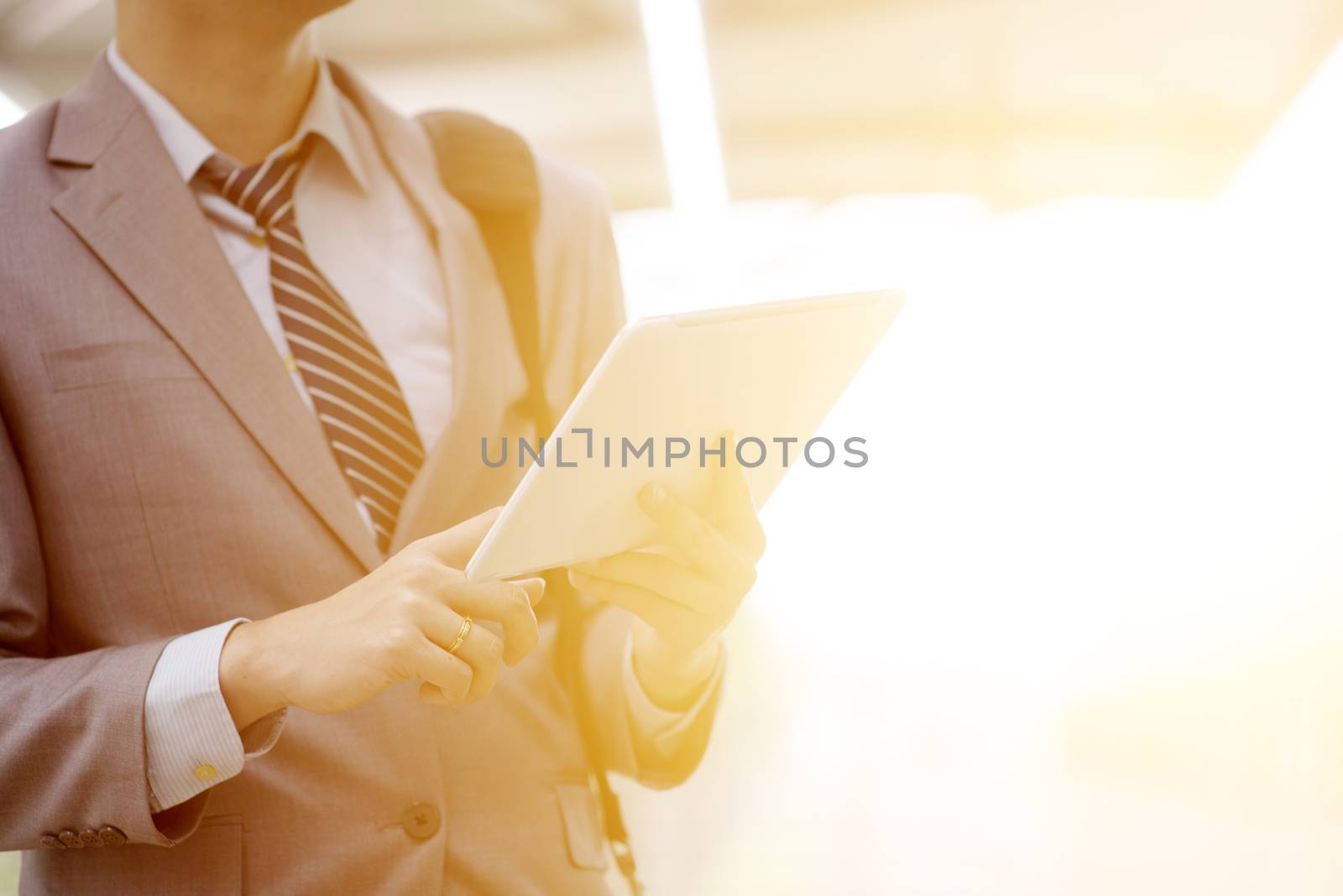 Businessman hand using digital tablet pc at railway station, with beautiful sun flare at background.