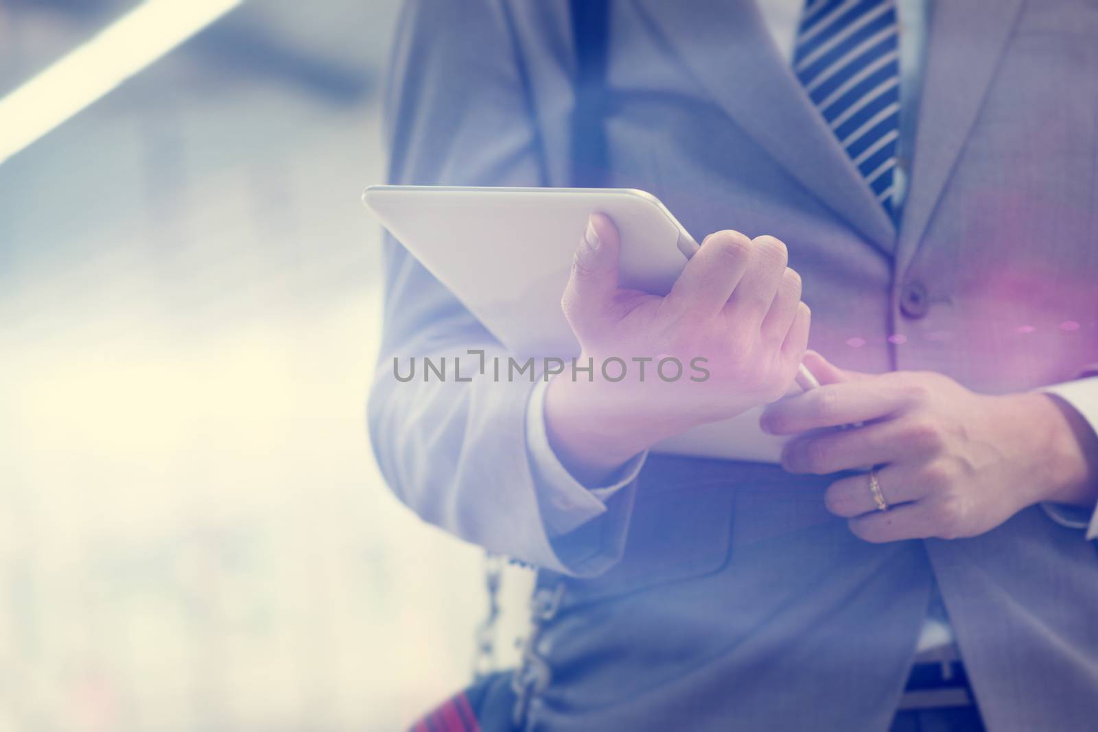 Businessman hand holding digital tablet pc at train station, with beautiful sun flare at background.