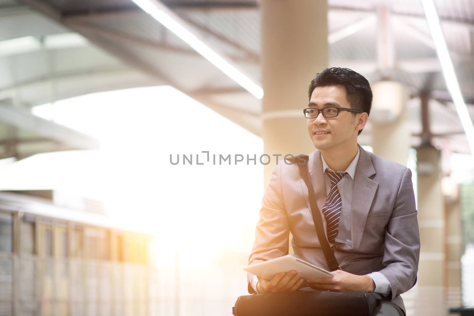 Asian businessman using digital tablet pc at commuter station, with beautiful sun flare at background.