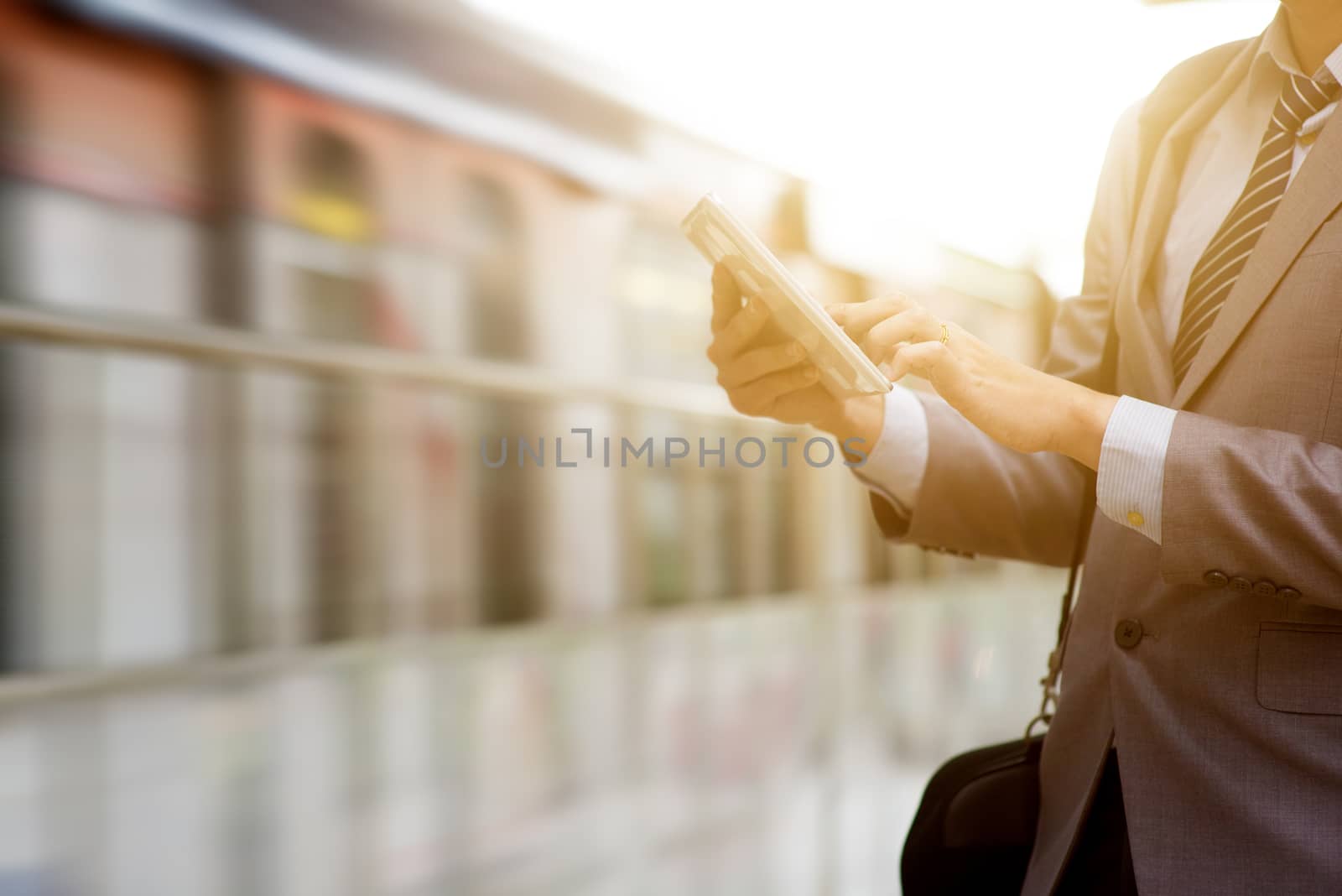 Businessman hand using digital tablet pc at train station, with beautiful sun flare at background.