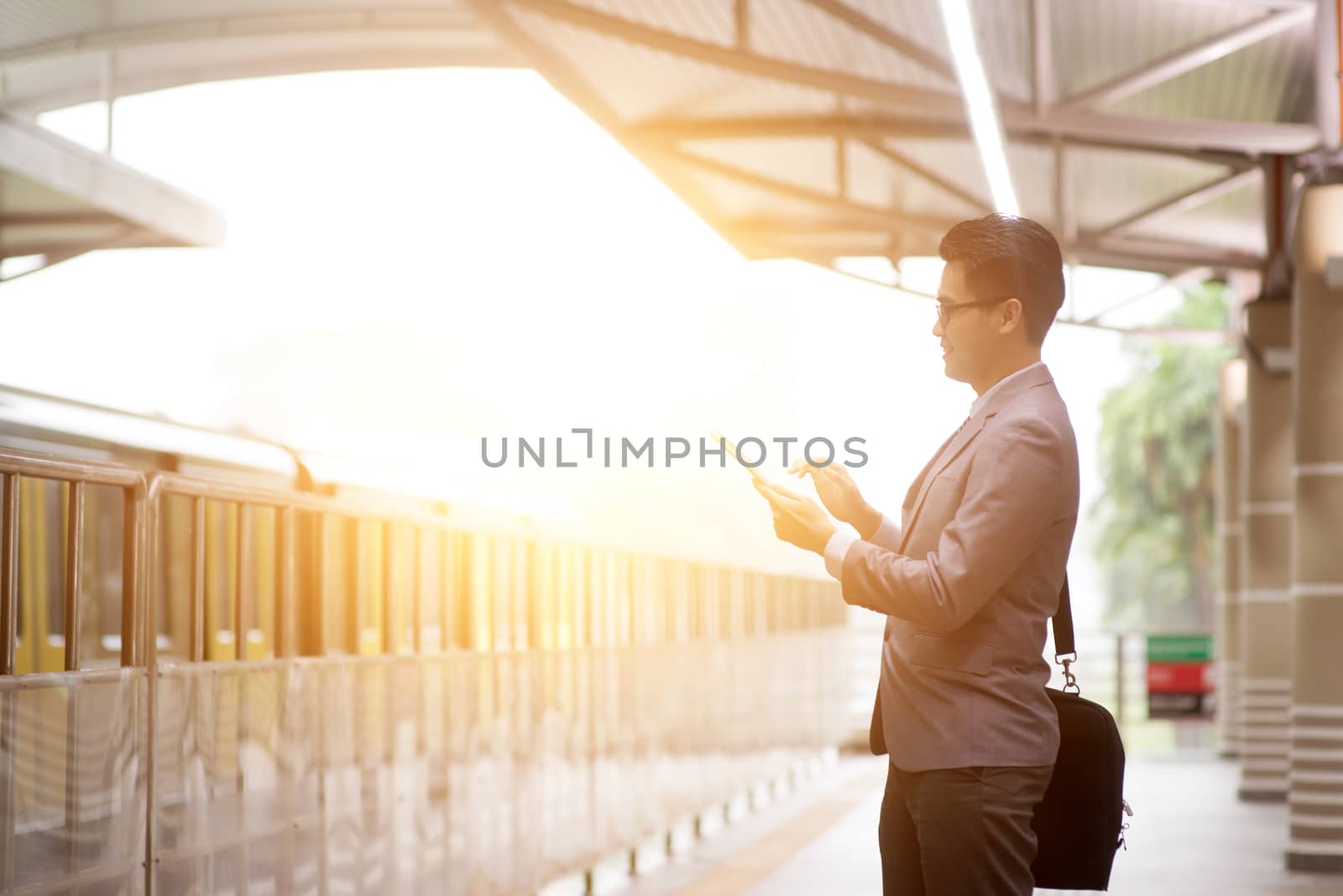 Asian businessman using digital tablet pc at transit platform, with beautiful sun flare at background.