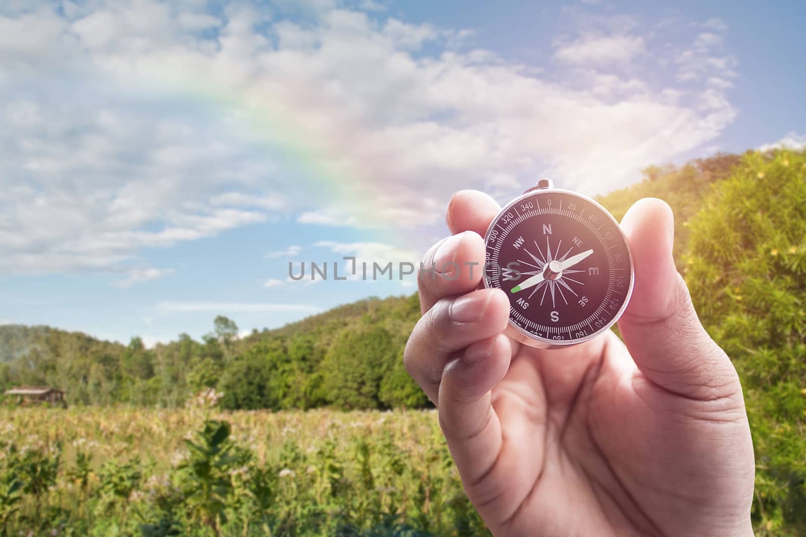 Compass in hand on blur of mountain view with rainbow for background