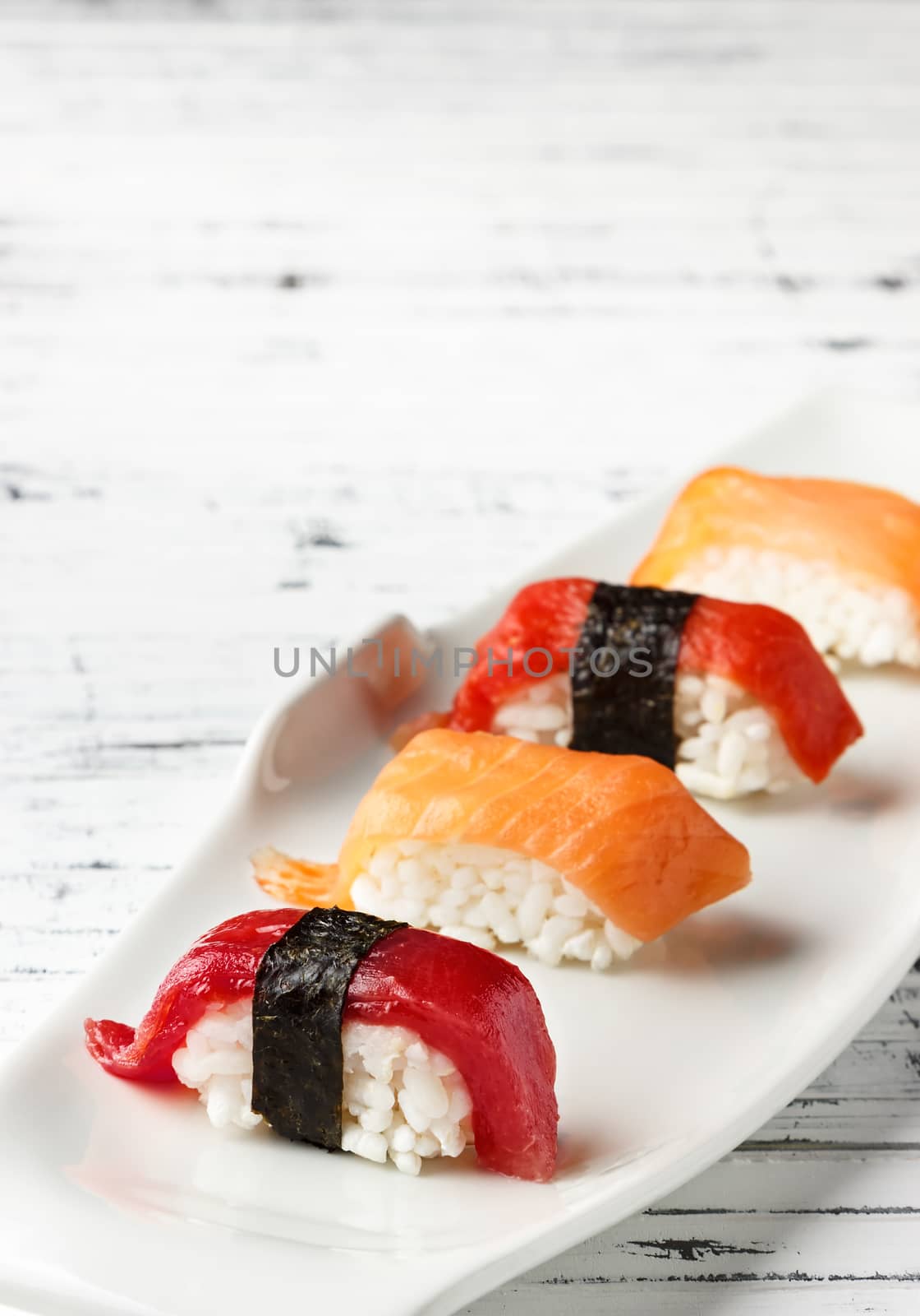  Set of salmon and red tuna Nigiris on white plate over old white wood. Raw fish in traditional Japanese sushi style. Vertical image.