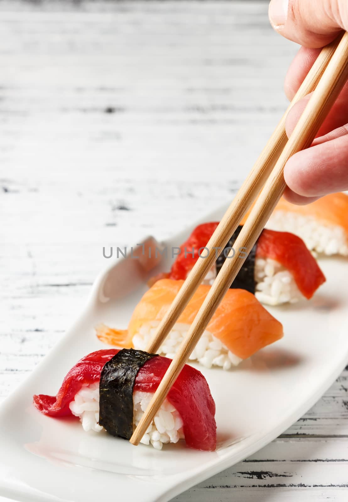  Set of salmon and red tuna Nigiris on white plate over old white wood with chopsticks. Raw fish in traditional Japanese sushi style. Vertical image.