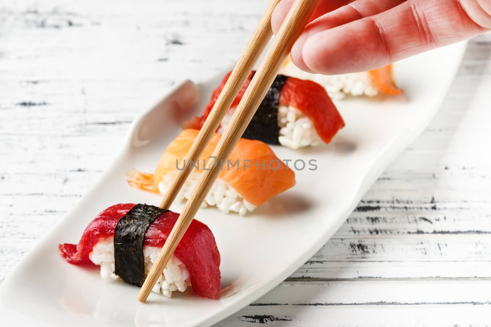  Set of salmon and red tuna Nigiris on white plate over old white wood with chopsticks. Raw fish in traditional Japanese sushi style. Horizontal image.