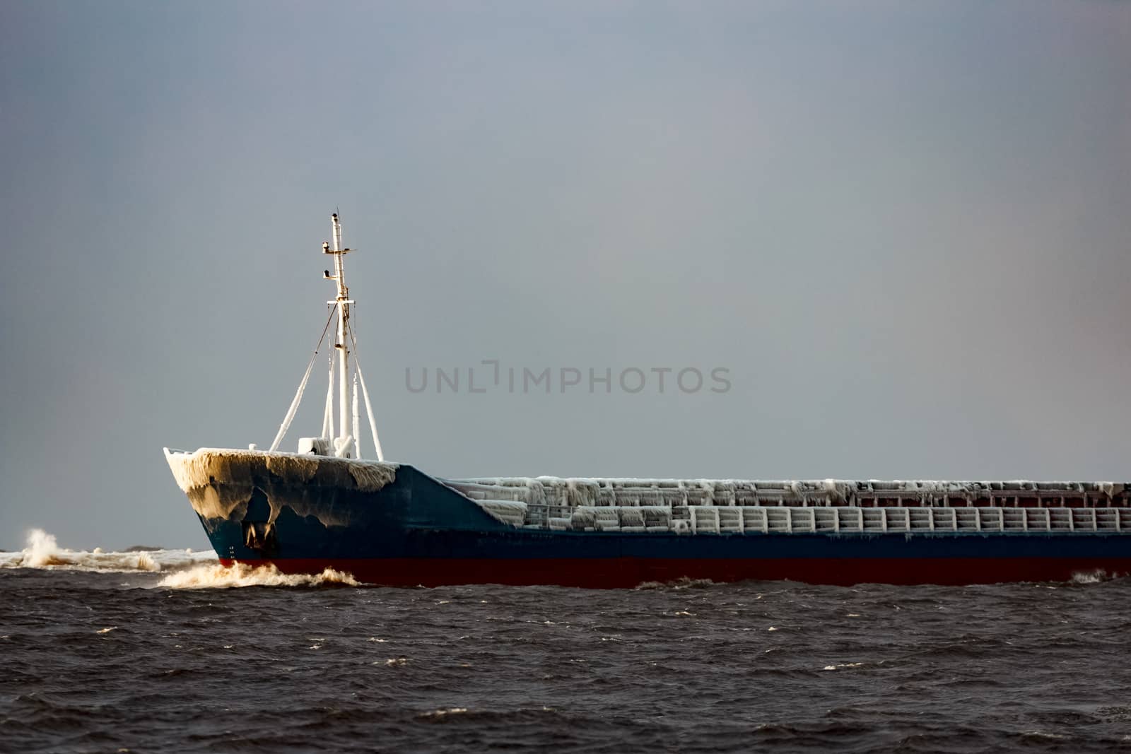 Blue bulk carrier moving from the sea in cold winter