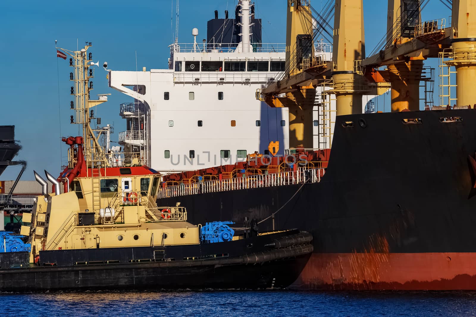 Black cargo ship mooring at the port with tug ship support