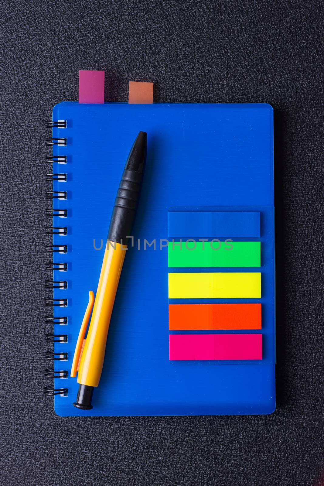 Blue notepad with multi-colored stickers and pen on a black background