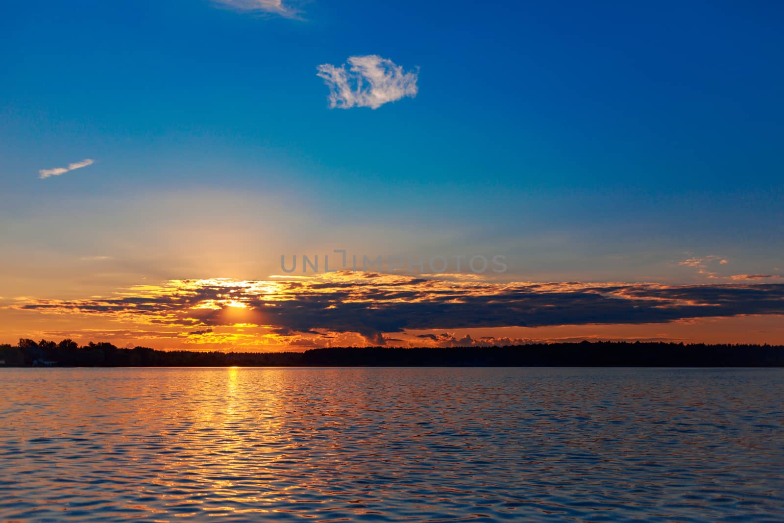 Pink-yellow sunset and sun reflection on lake water surface.
