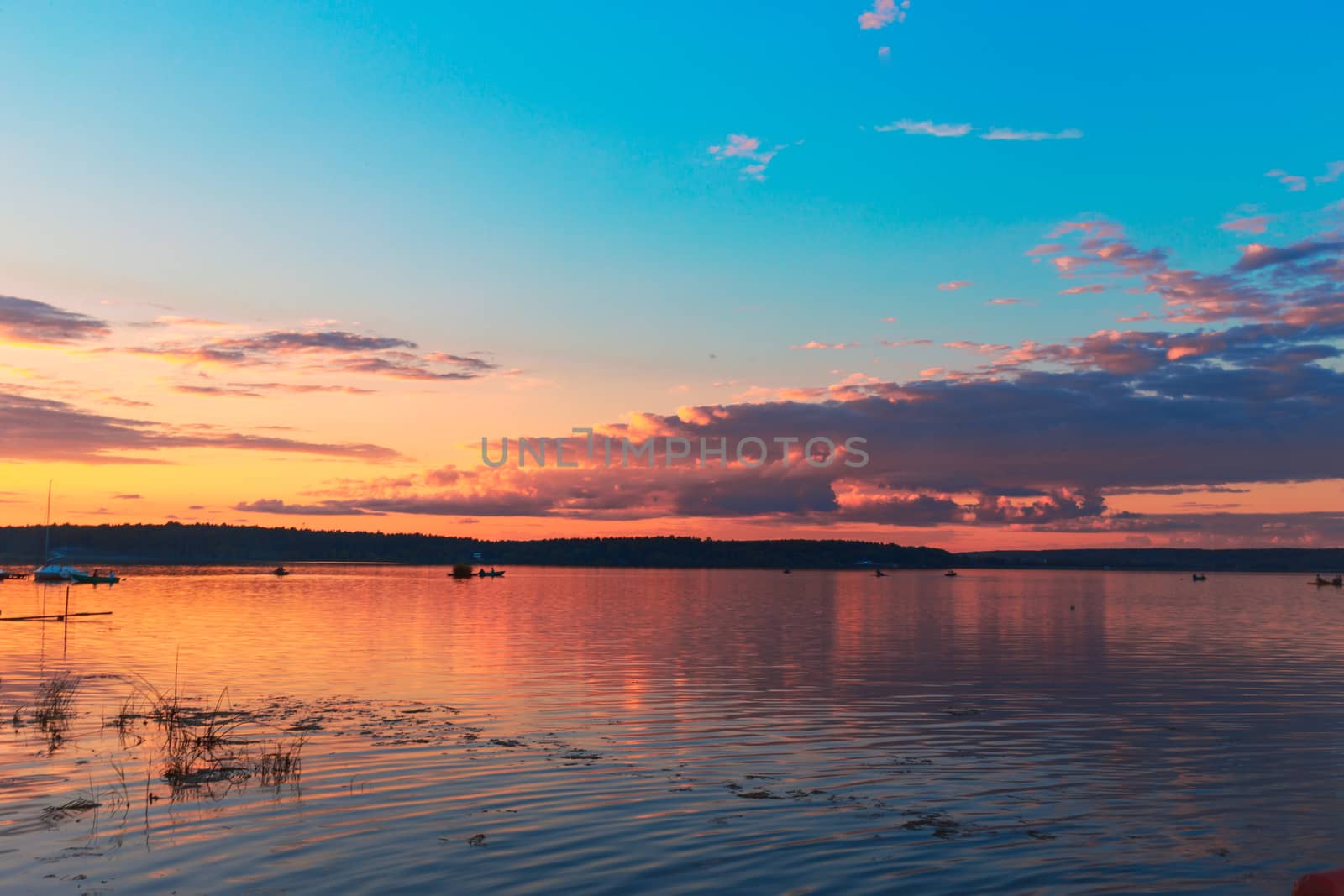 Pink-yellow sunset and sun reflection on lake water surface.