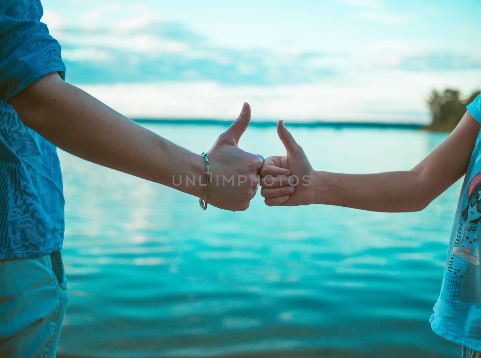 Two young women holding thumbs up on the lake in the summer