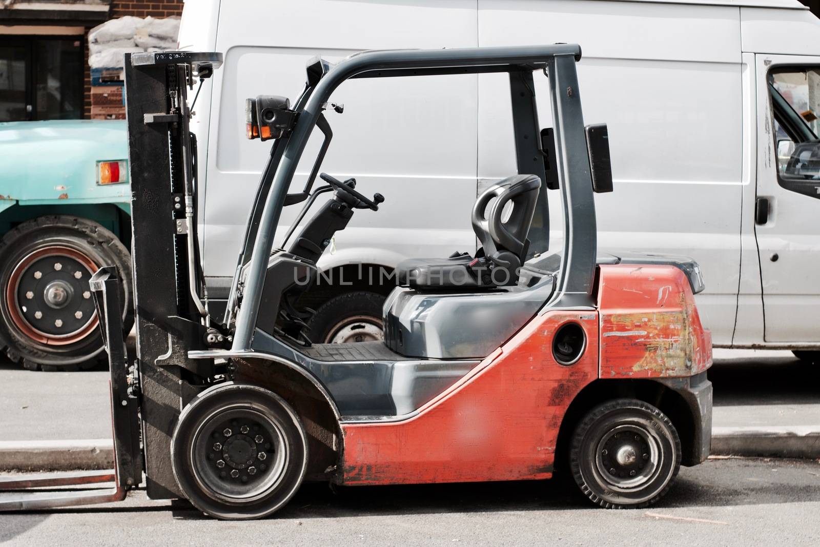 Old red outdoor lift truck near white big van and blue reach truck.