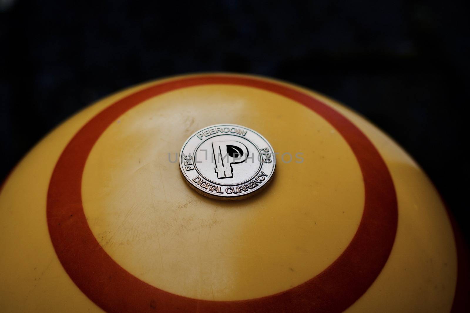 Digital currency physical gold peercoin coin on yellow circle background.