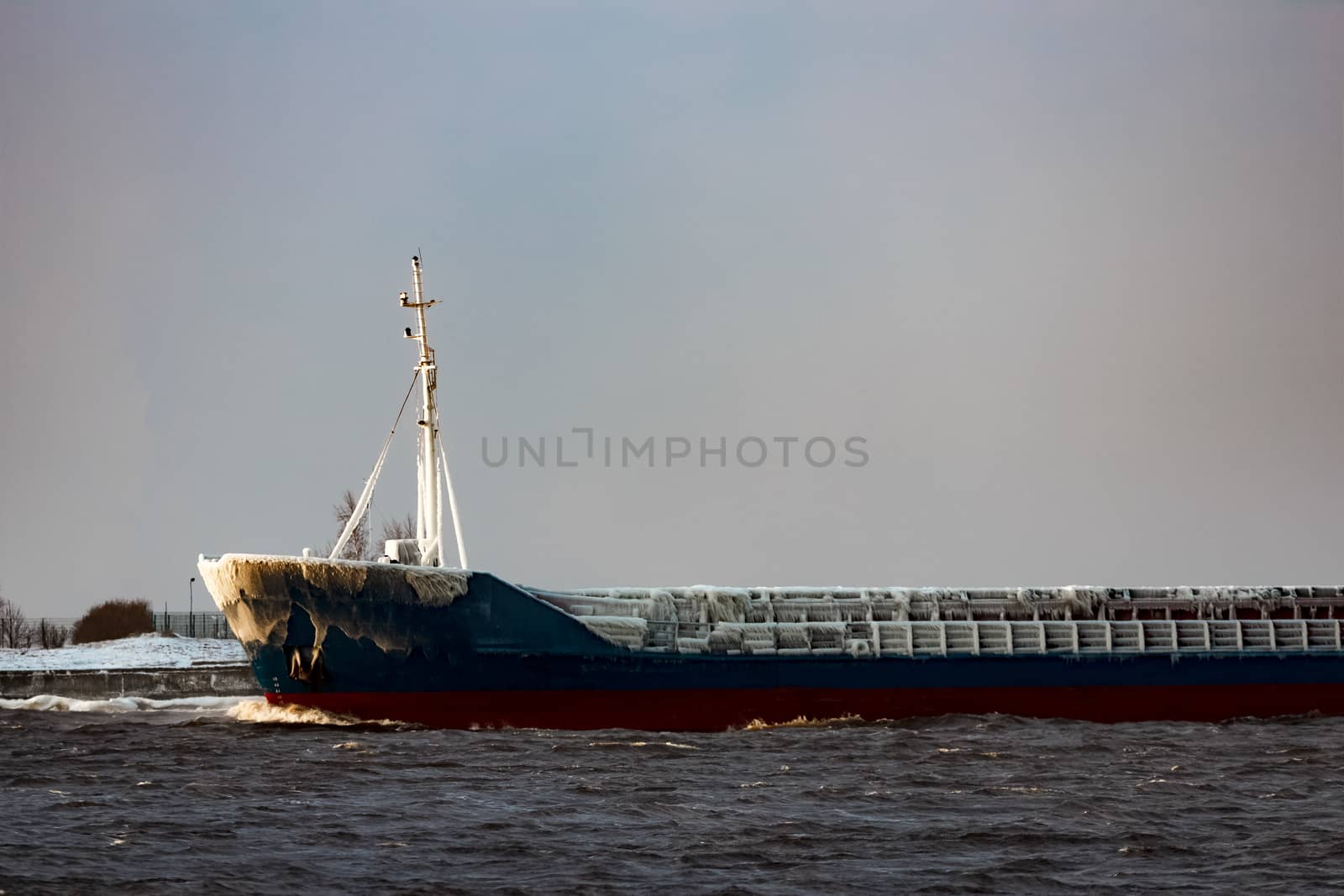 Blue bulk carrier moving from the sea in cold winter