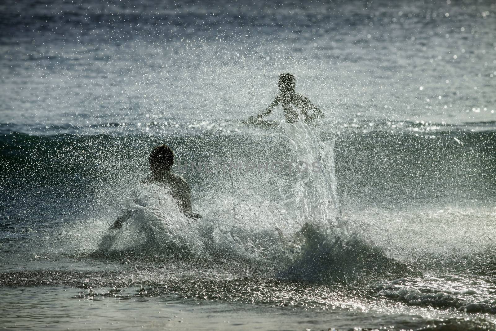 Silhouettes of people in the splashes of the ocean at sunset