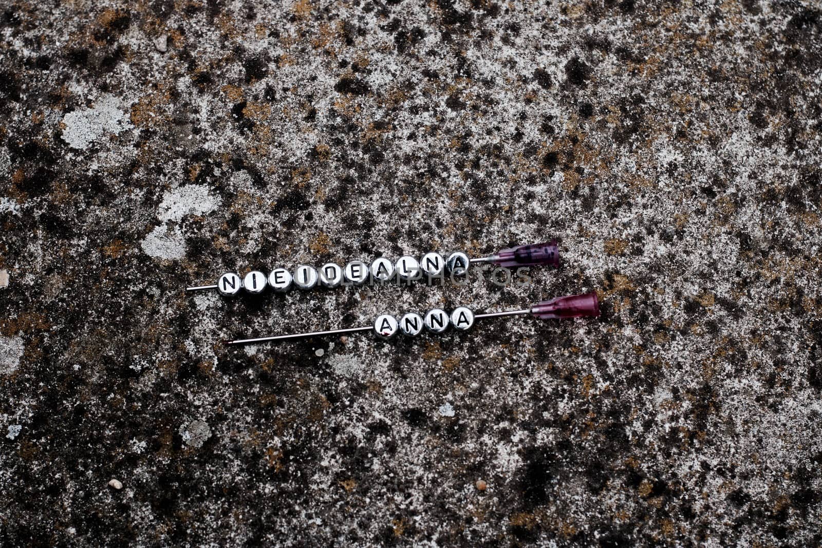 Two needles with sign. Nieidealna Anna on the dirty background.