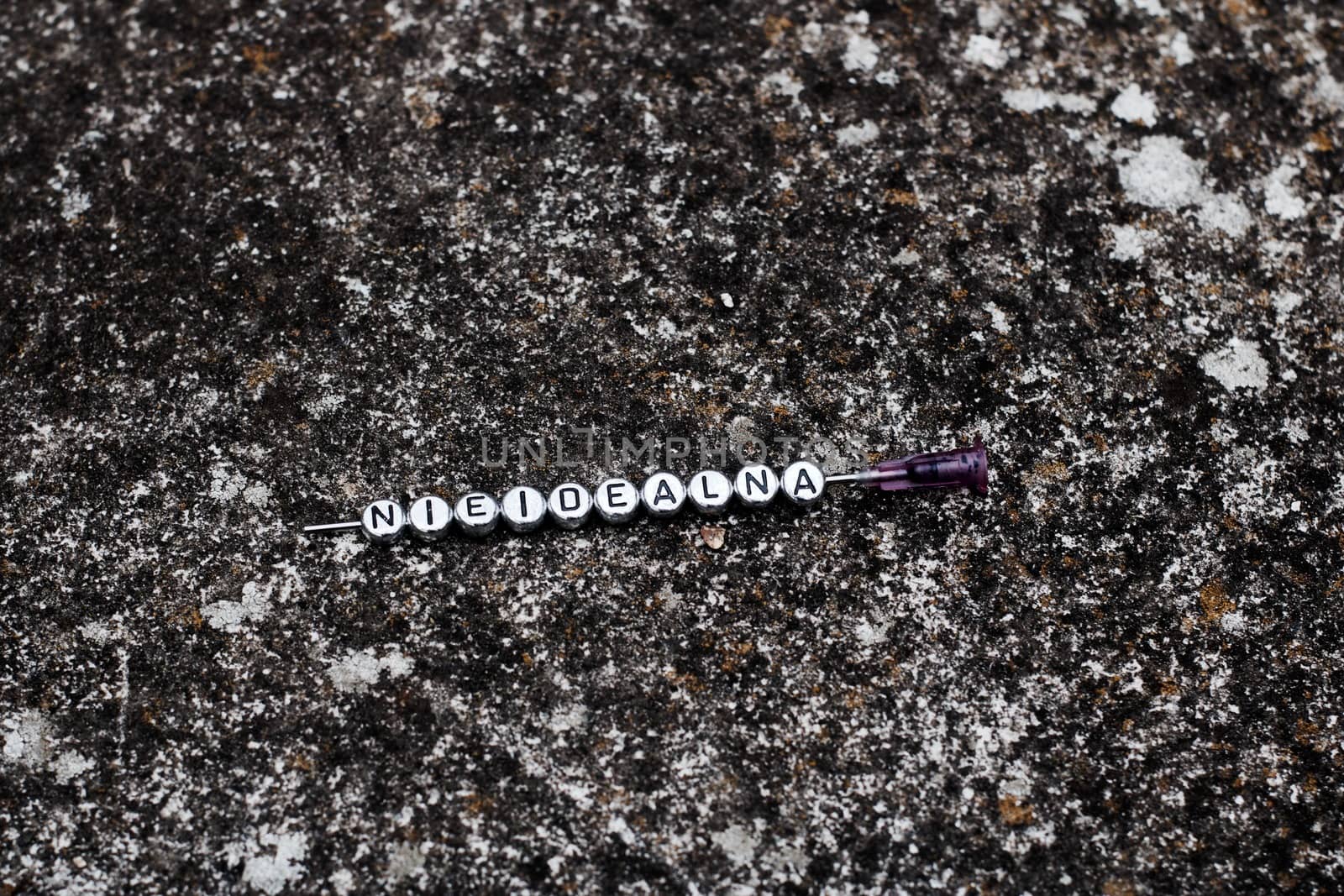 Small silver letters on the needle in dirty dark background. Nieidealna.