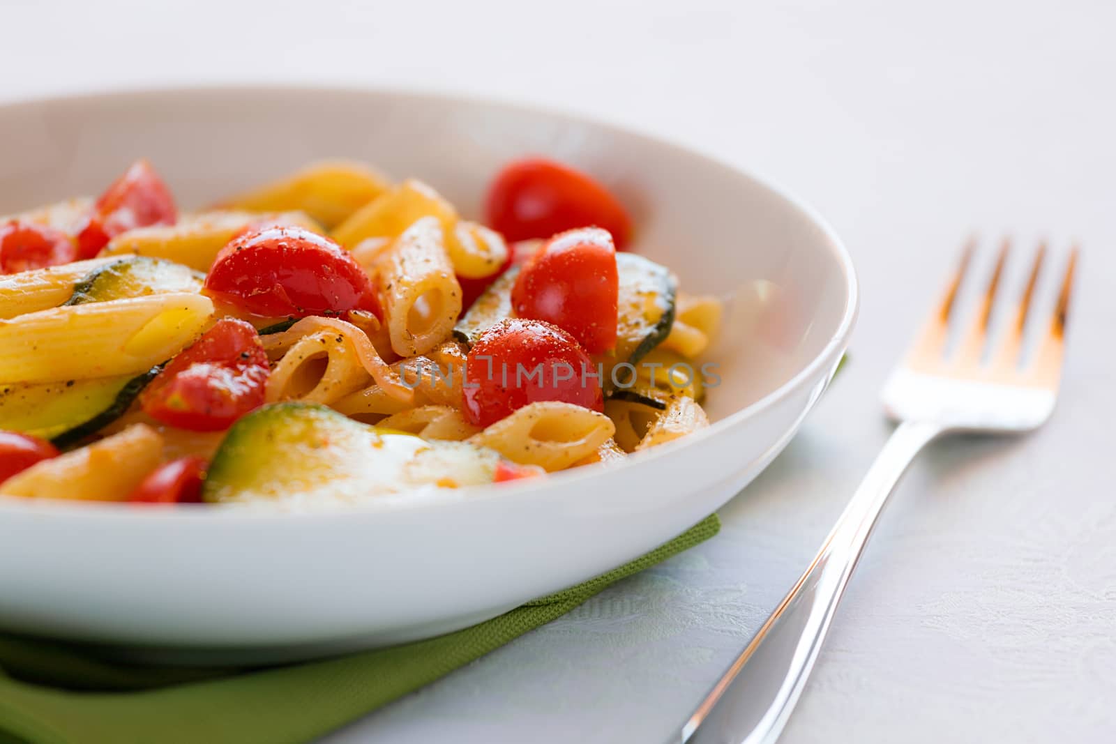 Closeup of traditional italian penne pasta with zucchini and cherry tomatoes seasoned with oil and black pepper