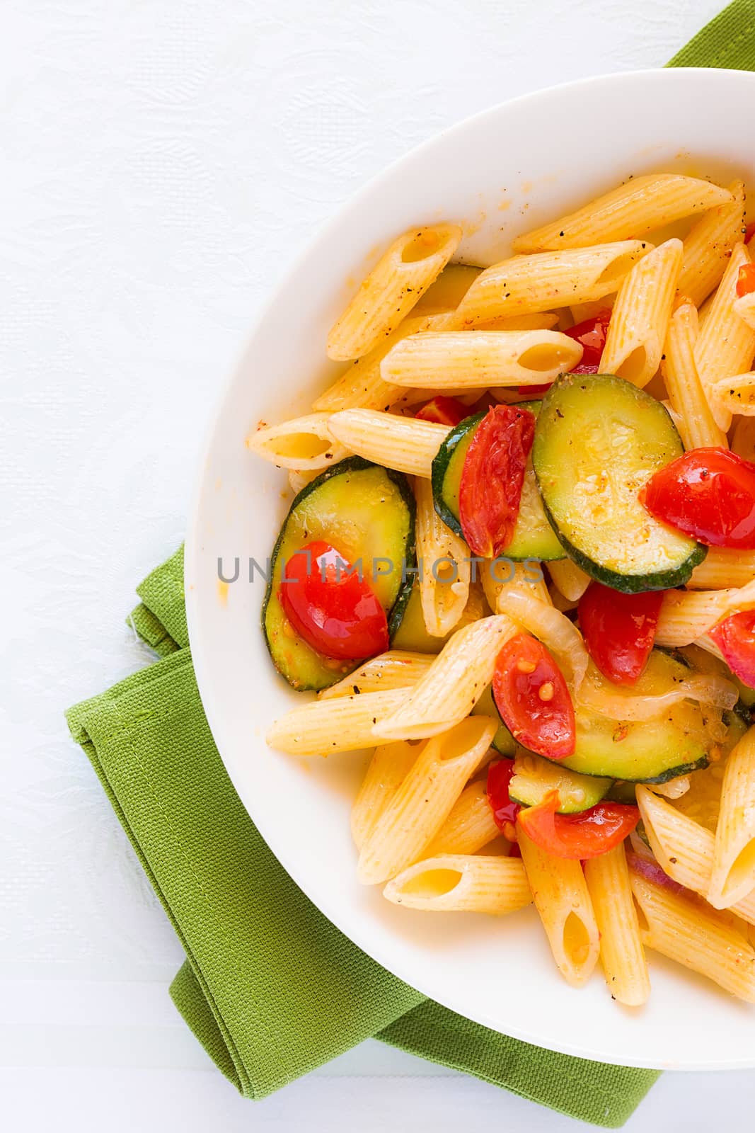 Closeup of traditional italian penne pasta with zucchini and cherry tomatoes seen from above