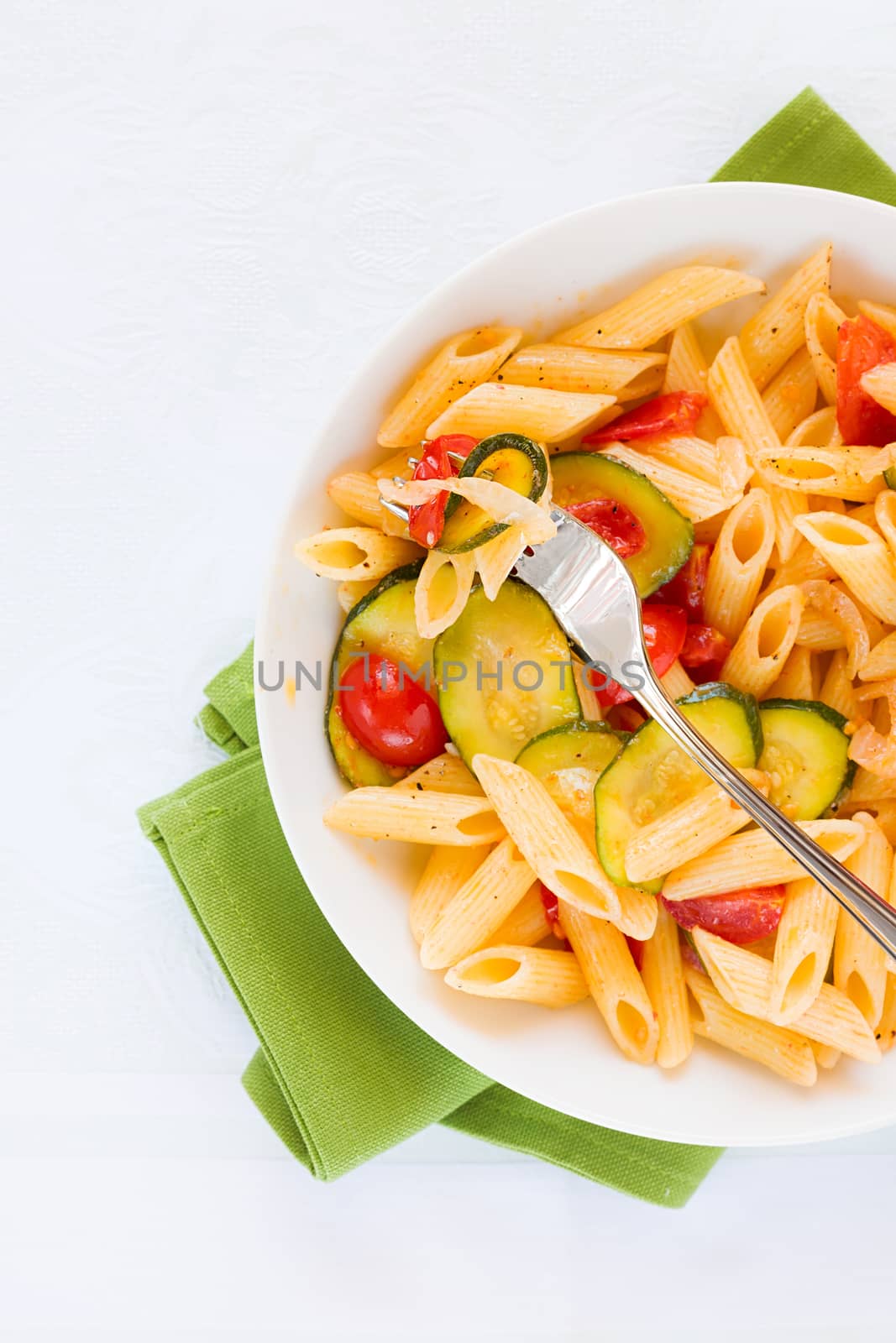 Traditional italian penne pasta with zucchini and cherry tomatoes seasoned with oil and black pepper seen from above