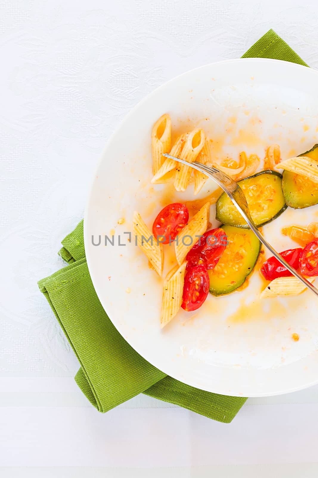 Traditional italian penne pasta with zucchini and cherry tomatoes already eaten seen from above