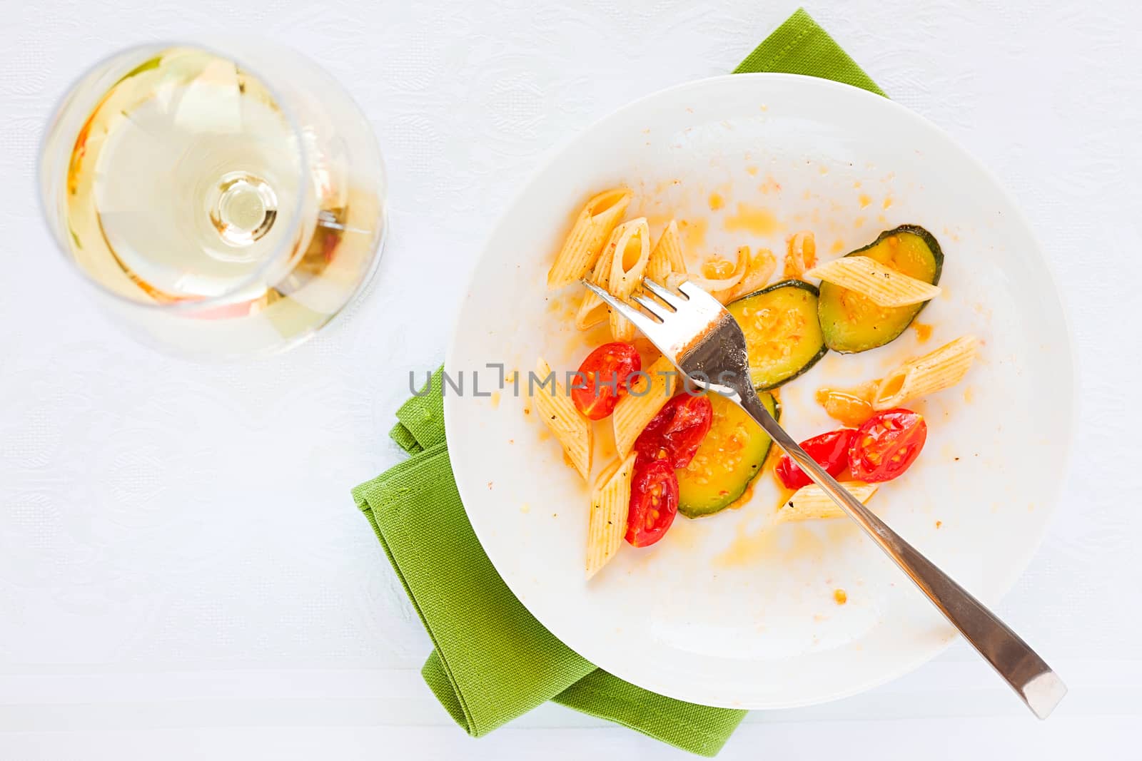 Traditional italian penne pasta with zucchini, cherry tomatoes and glass of white wine seen from above