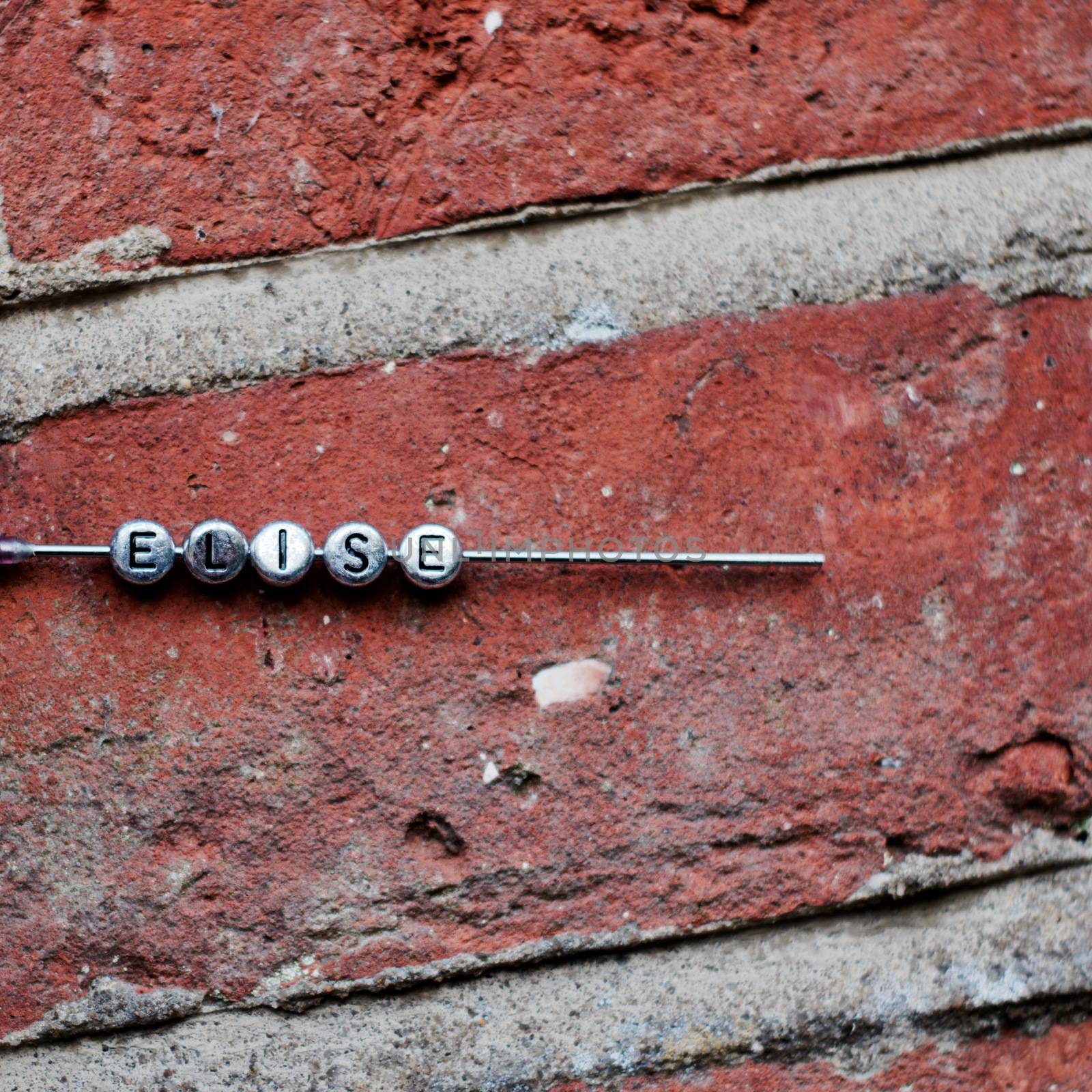 Small silver pins letters Elise on the needle. Brown brick dirty background.