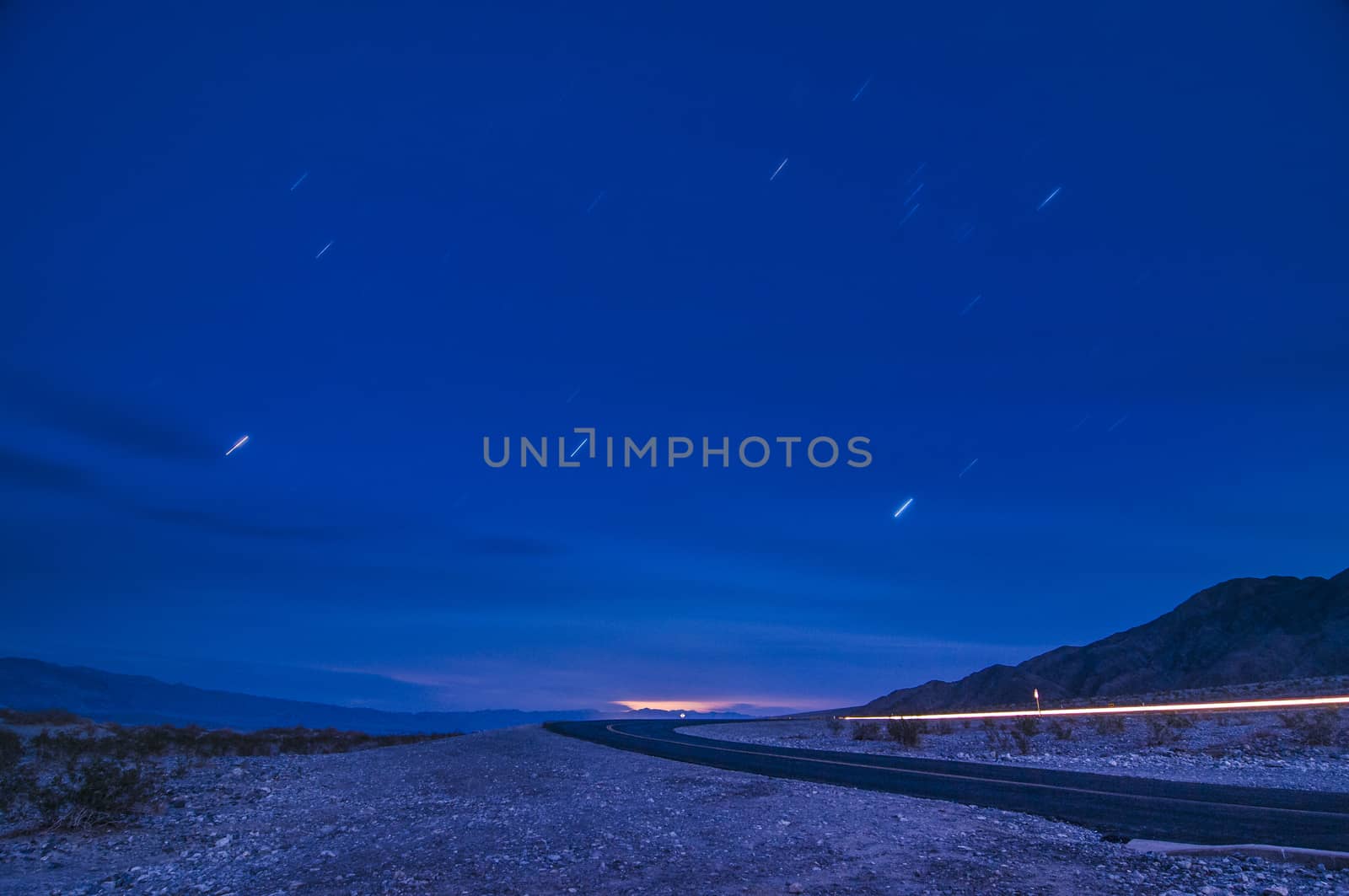 Moonlit road with car's headlight trails and star-trails in Death Valley, California