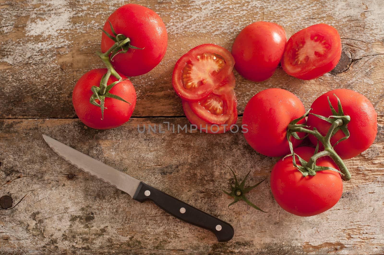 Preparing fresh tomatoes for a salad or cooking with an overhead view of ripe cherry tomatoes and a kitchen knife on an old chopping board