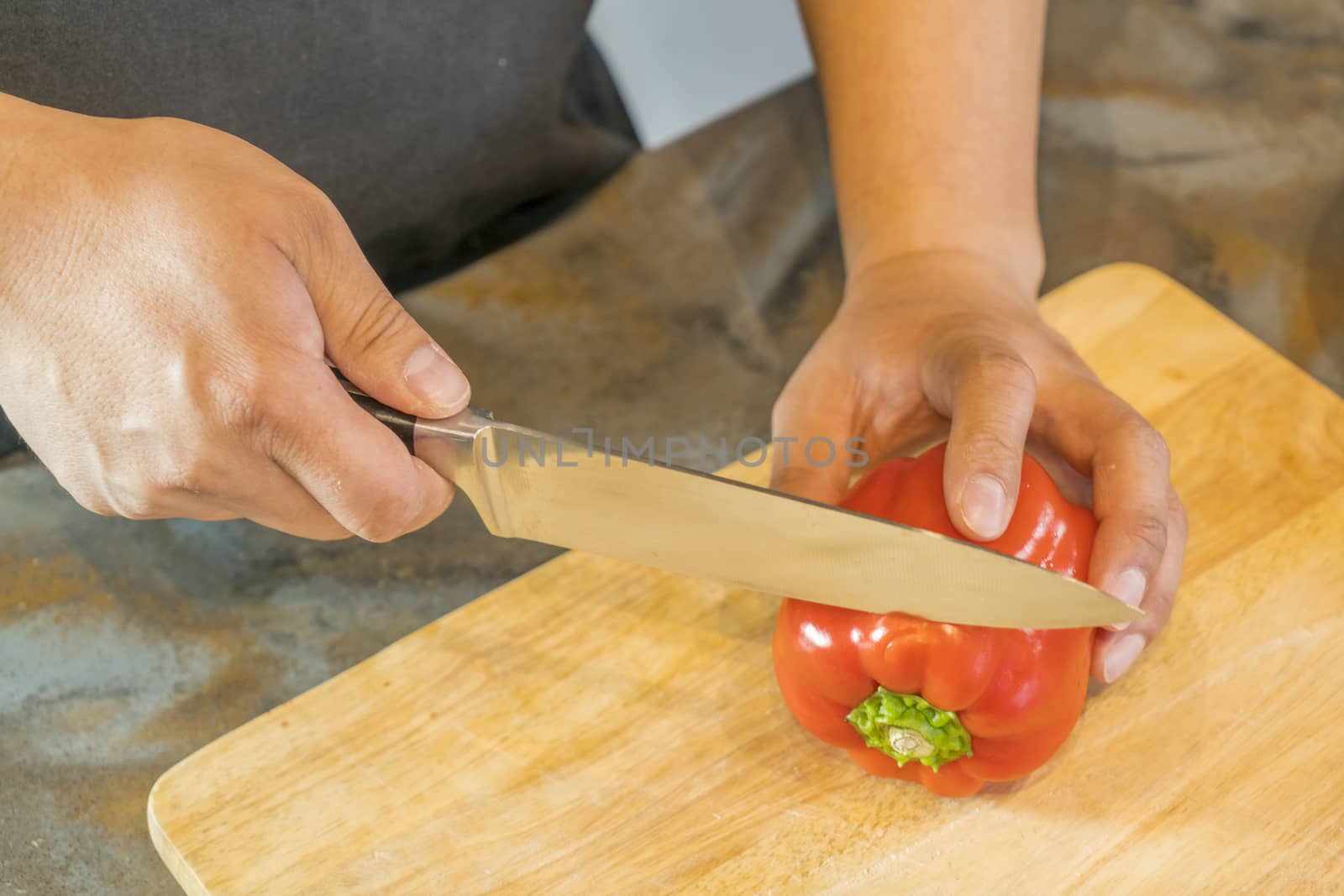 Chef cutting red bell pepper on wooden broad.