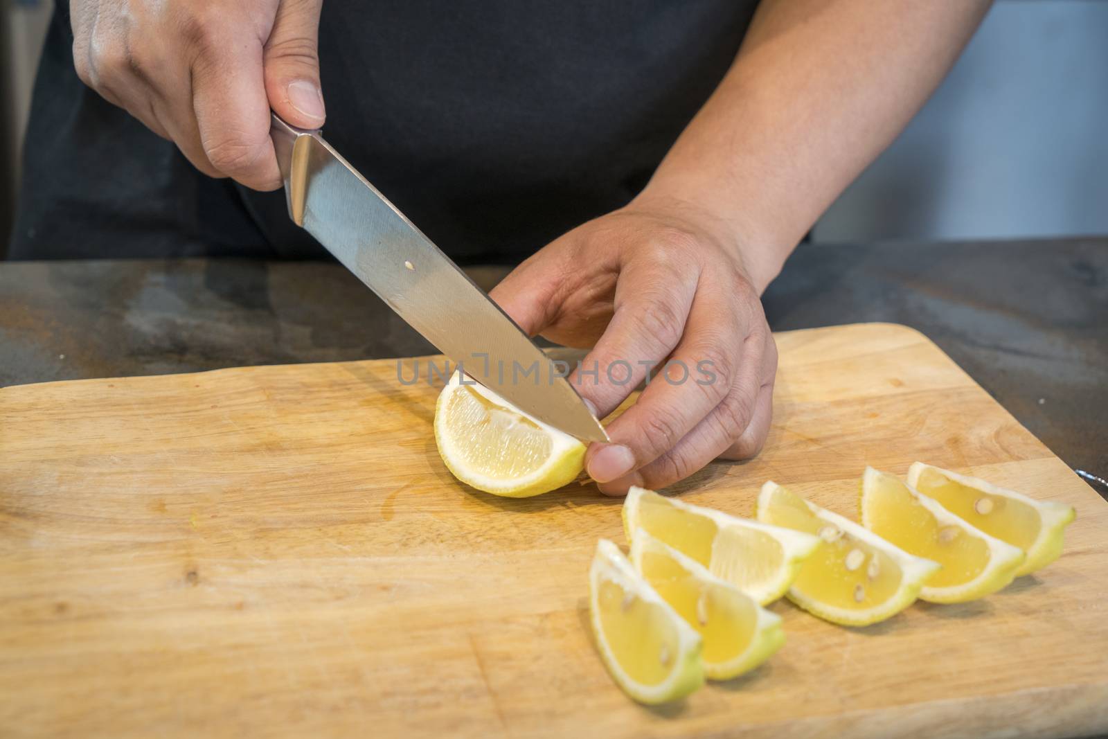 Chef slicing Lemon on wooden cutting board.