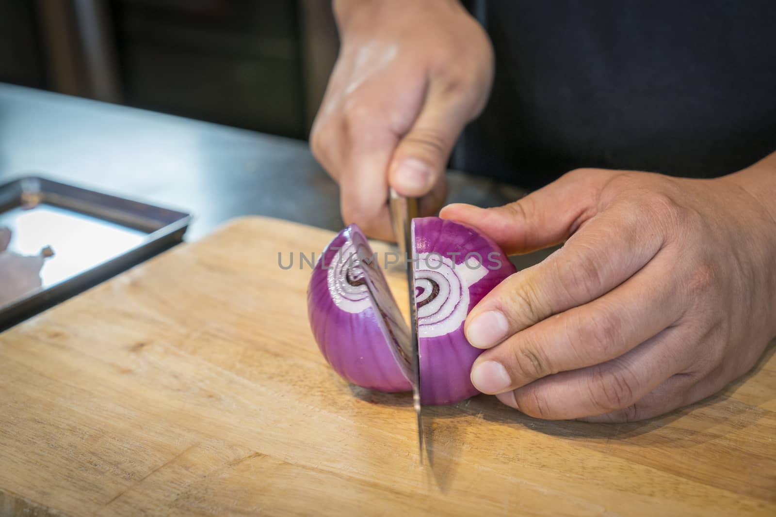Chef chopping a red onion with a knife on the cutting board.