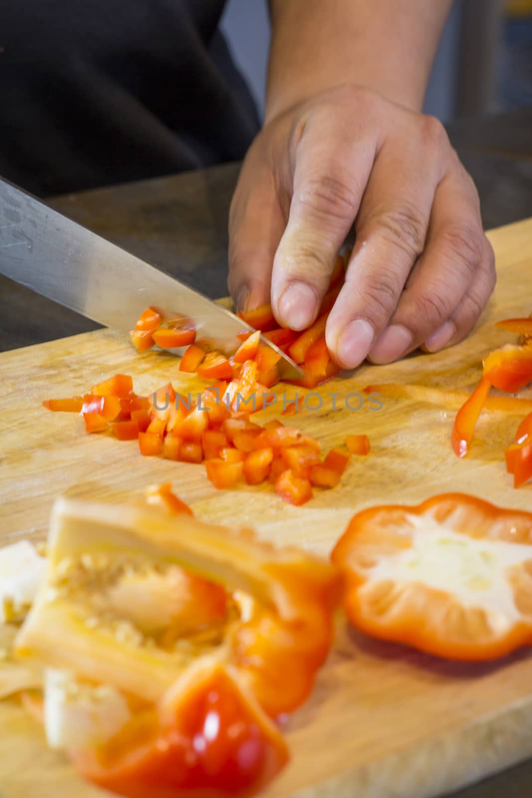 Chef cutting red bell pepper on wooden broad.