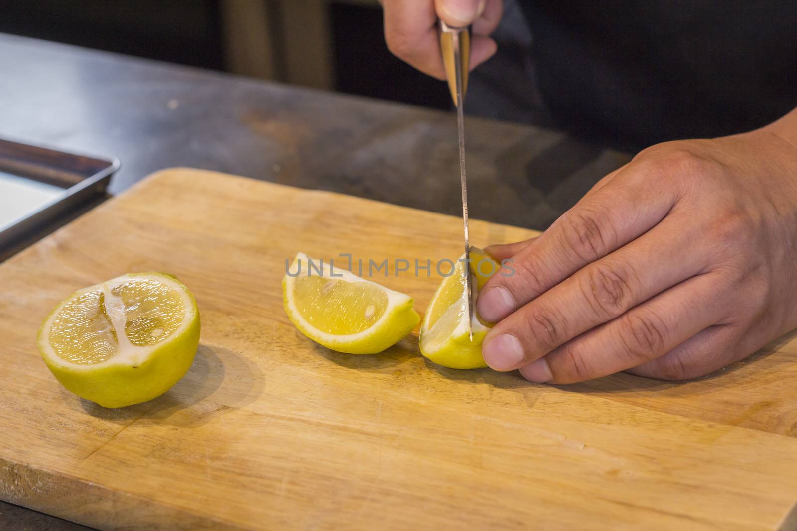 Chef slicing Lemon on wooden cutting board.