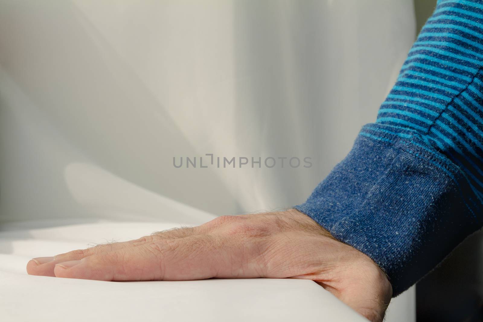 Man leaning and puts his hands down on white cloth background.