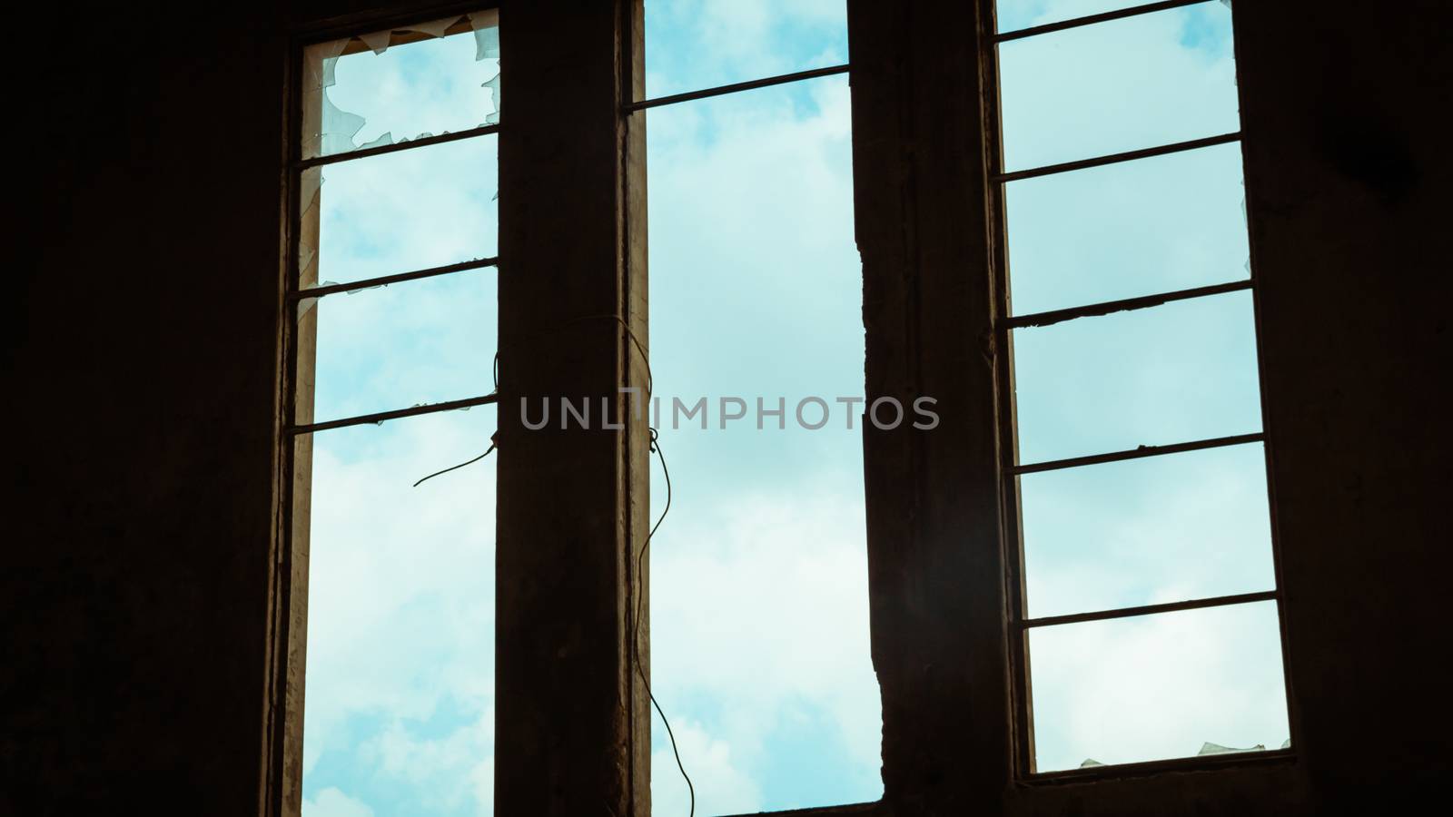 Broken window in an abandoned building - View from inside - sky with clouds seen through the window.