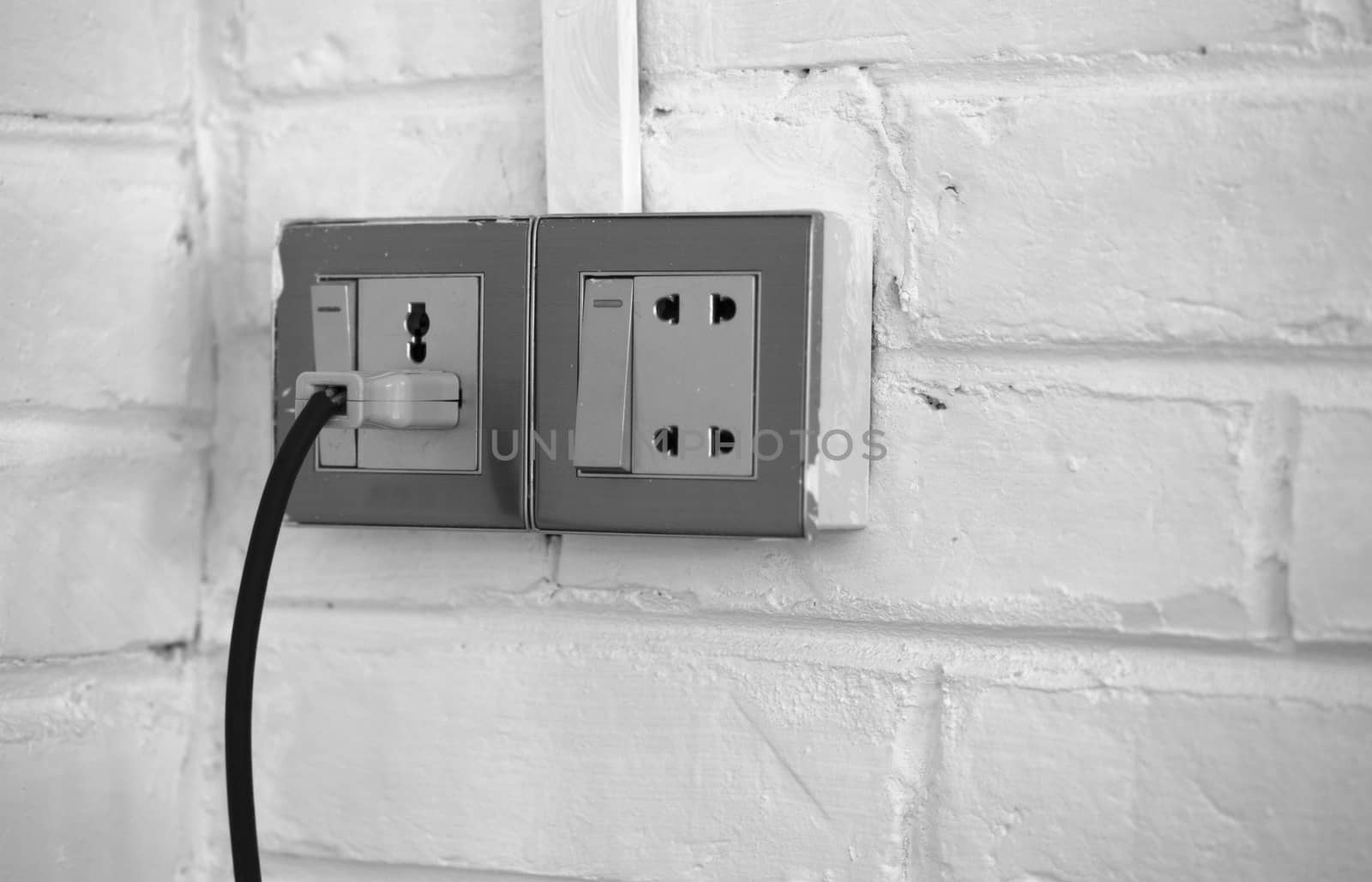 BLACK AND WHITE PHOTO OF PLUGGED OLD SOCKET ON WHITE BRICK WALL