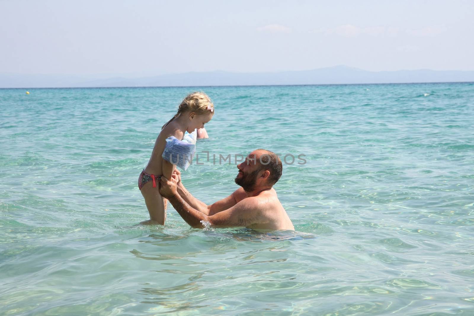 Father and daughter playing in the clear sea water