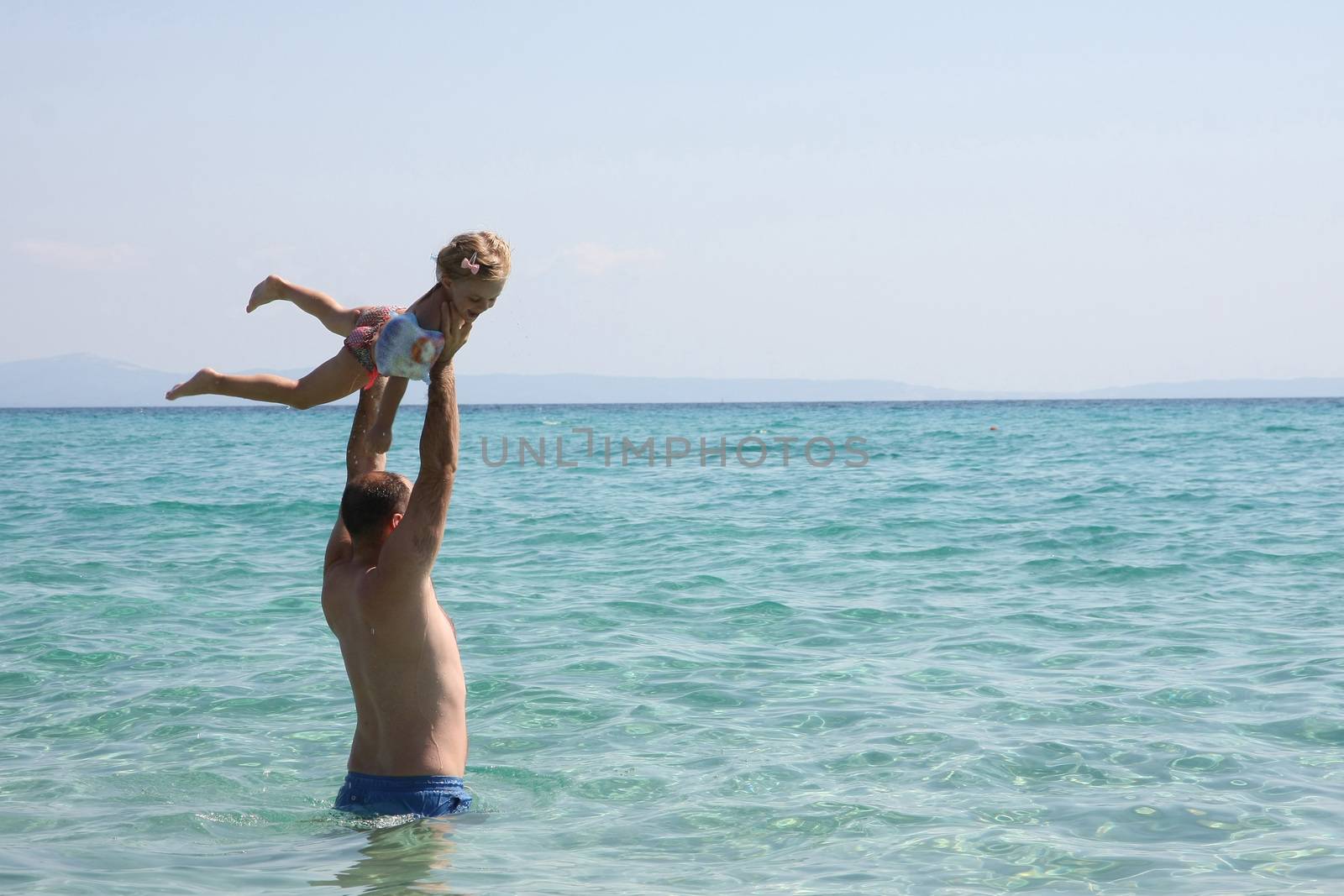 Father and daughter playing in the clear sea water