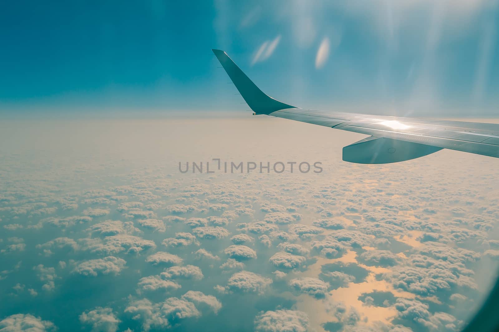 Wing of airplane from window at sunset. Many sheep clouds over the Mediterranean sea.