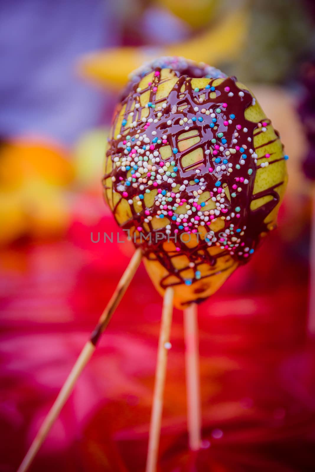 Pear on a stick coated chocolate with colored candies.